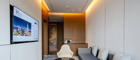 A modern hotel room with a sofa, a coffee table, a TV mounted on the wall, and a wooden accent wall.