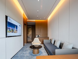 Una habitación de hotel moderna con un sofá, una mesa de centro, un televisor en la pared y una pared decorativa de madera.