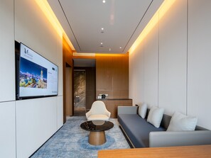 A modern hotel room with a sofa, a coffee table, a TV mounted on the wall, and a wooden accent wall. - Grand Madison Hotel Tangshan Caofeidian (Tangshan)