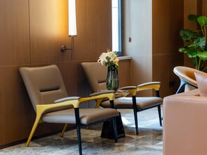 A modern waiting area with leather chairs, a marble floor, and a vase with flowers on a table. - Grand Madison Hotel Tangshan Caofeidian (Tangshan)