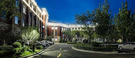 A well-lit urban street with a row of parked cars, a clear sky, and a building with multiple windows and a brick facade.