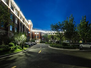 A well-lit urban street with a row of parked cars, a clear sky, and a building with multiple windows and a brick facade. - Grand Madison Hotel Tangshan Caofeidian (Tangshan)