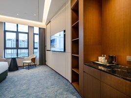 Una habitación de hotel con un ventanal grande, una cama, un escritorio, una silla, un televisor y un minibar.