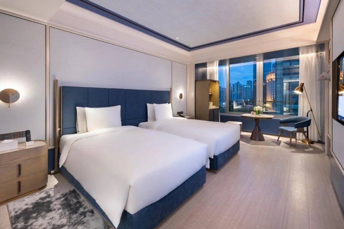 Une chambre d’hôtel moderne avec deux lits, une vue sur la ville, un bureau et une table de chevet.