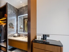 Un baño moderno con pared de mármol, armarios de madera, un espejo grande y una encimera con artículos de aseo.