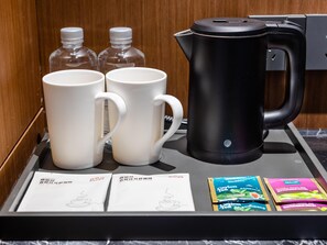 Un plat amb dues tasses blanques, una tetera elèctrica negra i sobres de te.