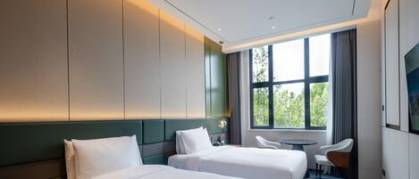 A hotel room with two beds, a desk, a chair, and a large window with a view of trees.