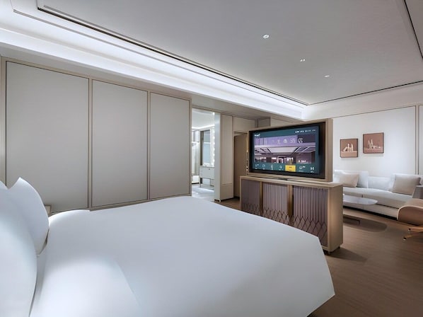 A modern hotel room with a large bed, a flat-screen TV mounted on a wooden console, a white sofa, and a minimalist decor.