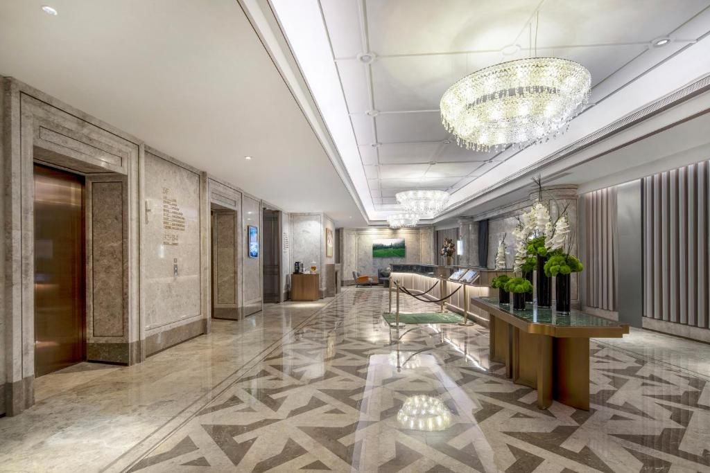 A modern hotel lobby with a geometric patterned floor, a reception desk with a glass top, and a large chandelier.