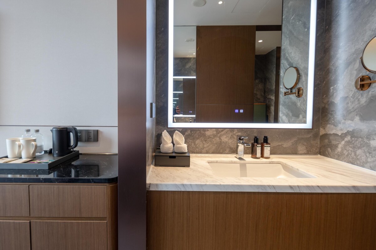 A modern bathroom with a large mirror, a sink, and a countertop with toiletries.