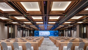 A conference room with rows of tables and chairs, a large screen at the front, and a patterned carpet. - Grand Madison Hotel Tangshan Caofeidian (Tangshan)
