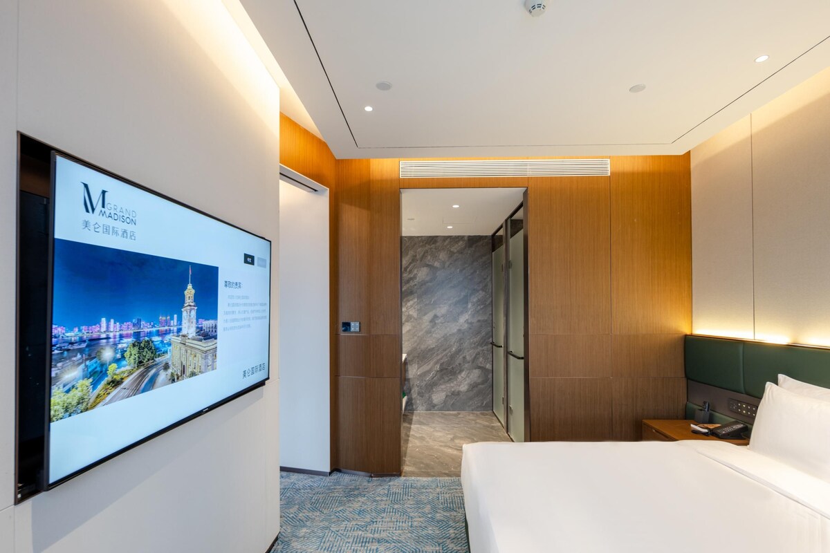 Une chambre d’hôtel avec un grand lit, un téléviseur fixé au mur et un espace douche.