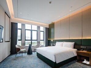 Habitación de hotel moderna con una cama grande, un escritorio, una silla y vistas a la ciudad a través de amplios ventanales.