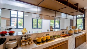 A modern kitchen with a marble countertop, various food items, and a view of the outside. - Grand Madison Hotel Tangshan Caofeidian (Tangshan)