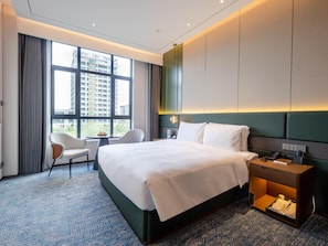 Habitación de hotel moderna con una cama grande, un escritorio, una silla y vistas de la ciudad a través de grandes ventanales.