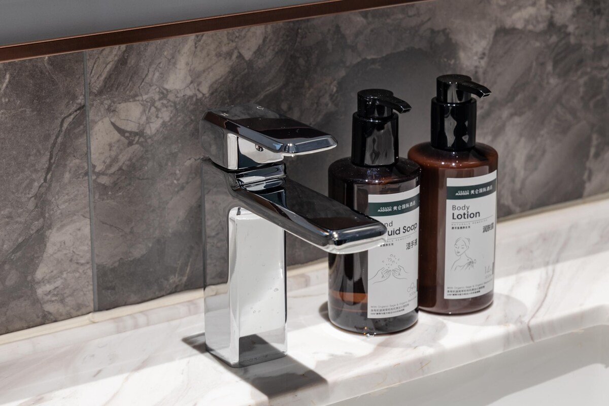 A bathroom with a chrome faucet, two bottles of liquid soap, and a bottle of lotion on a marble countertop.