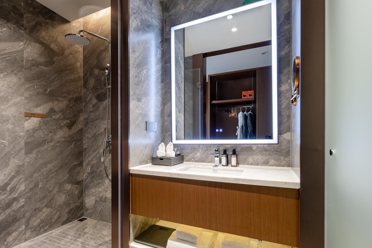 Un baño moderno con cabina de ducha de mármol, un espejo grande y un mueble de tocador de madera.