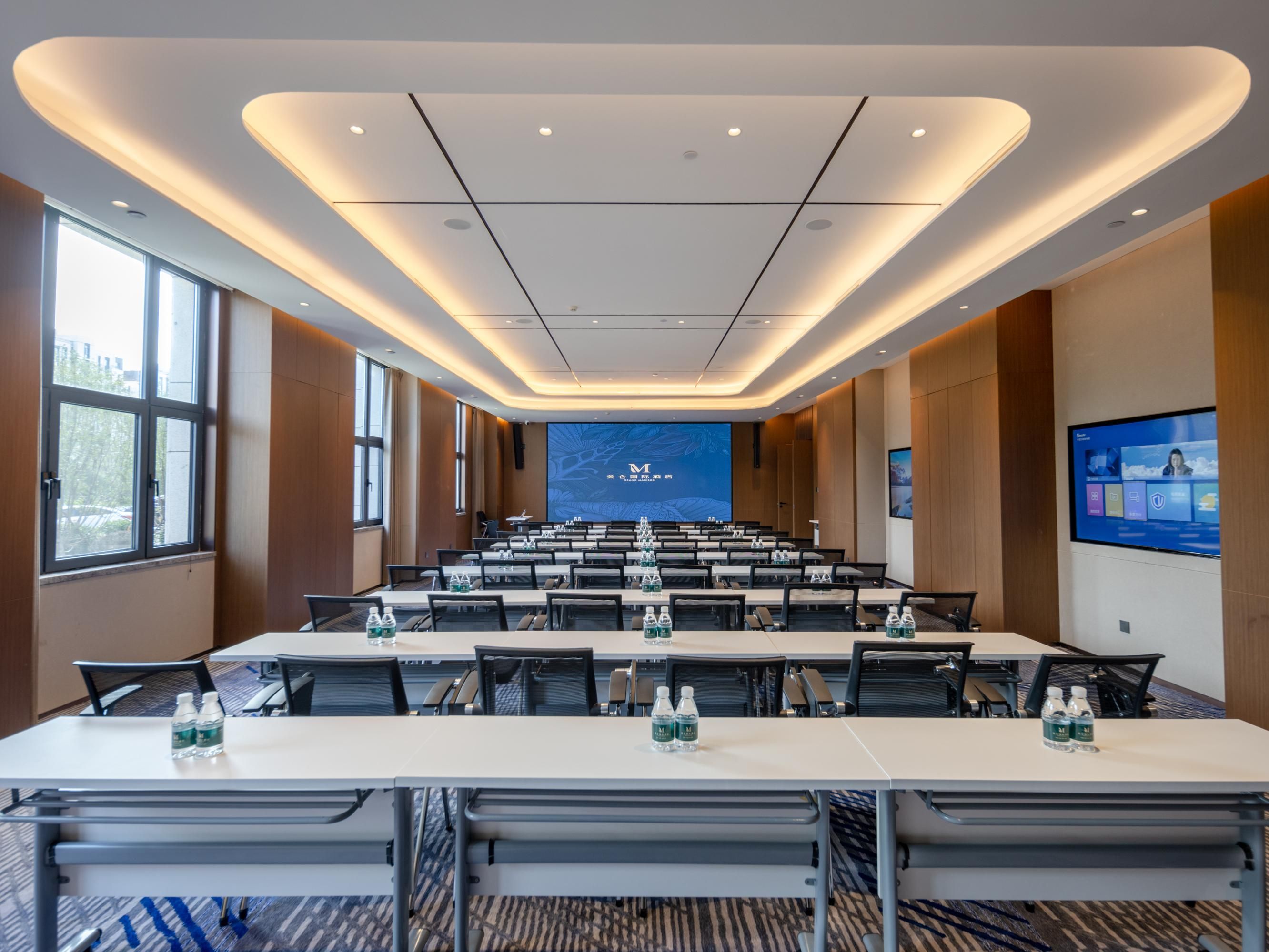 A conference room with a long table, chairs, and a large screen at the front.