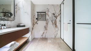 A modern bathroom with a marble wall, a vanity with a mirror, a towel rack, and a bench. - Grand Madison Hotel Nantong Tongzhou High-tech (Nantong)