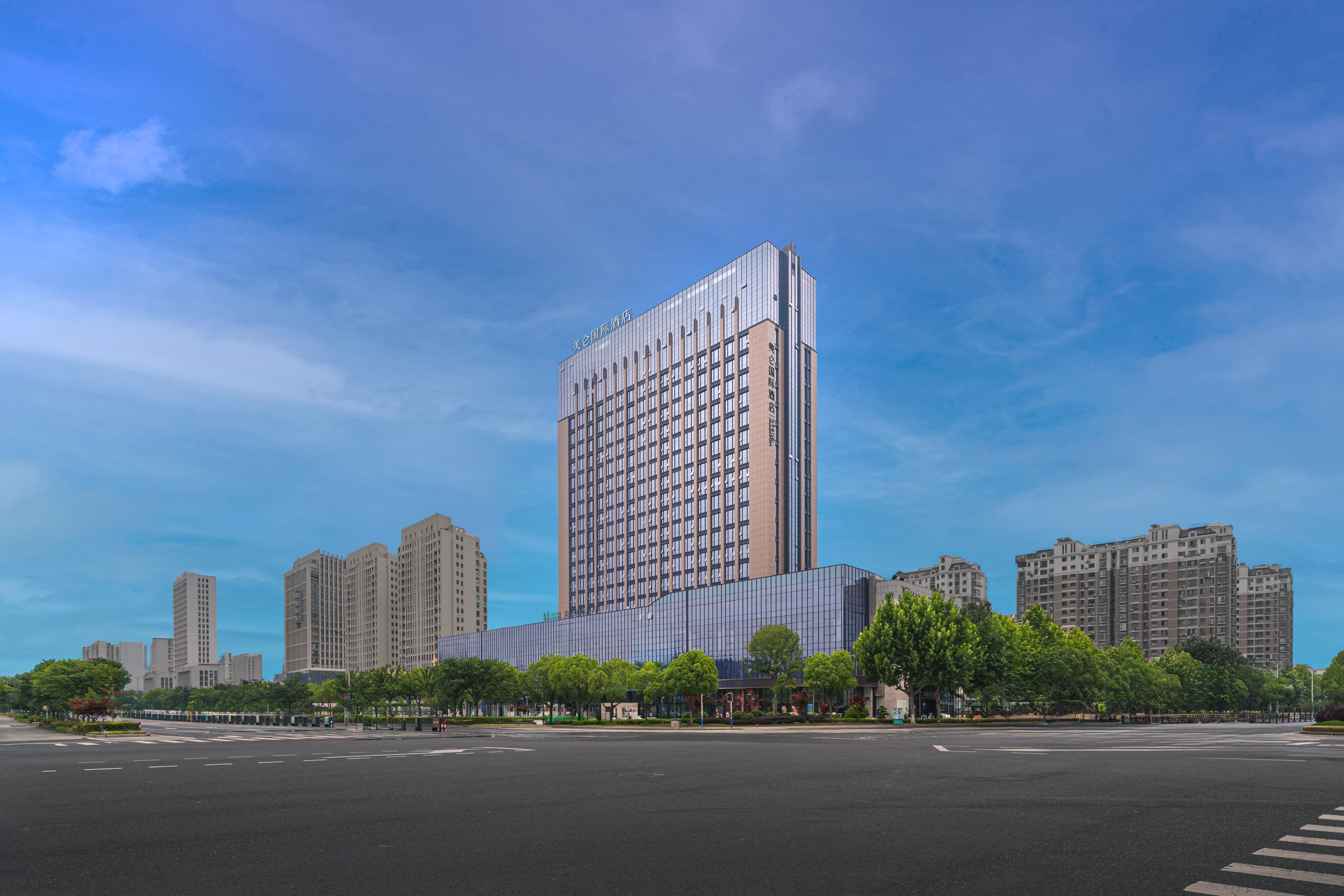 A modern high-rise building with a glass facade and a rectangular shape, surrounded by other high-rise buildings and a wide street.
