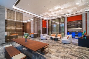 A modern lobby with a wooden reception desk, seating areas, and a display of bottles. - Grand Madison Hotel Nantong Tongzhou High-tech (Nantong)