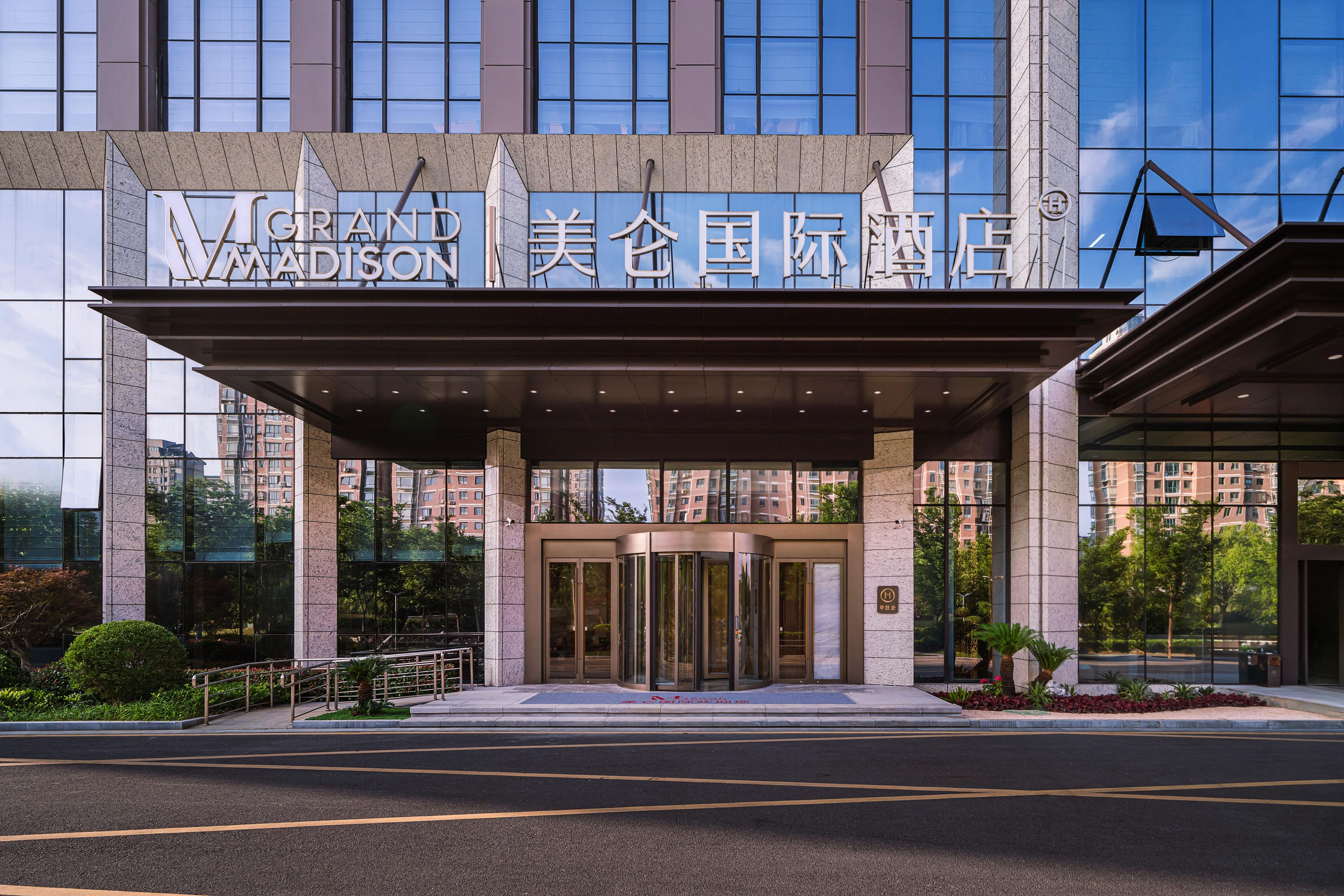 Entrada de hotel con puerta giratoria, ventanas grandes y un letrero en inglés y chino.