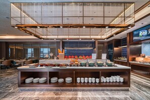 A modern hotel lobby with a buffet area, seating, and a large screen displaying content. - Grand Madison Hotel Nantong Tongzhou High-tech (Nantong)