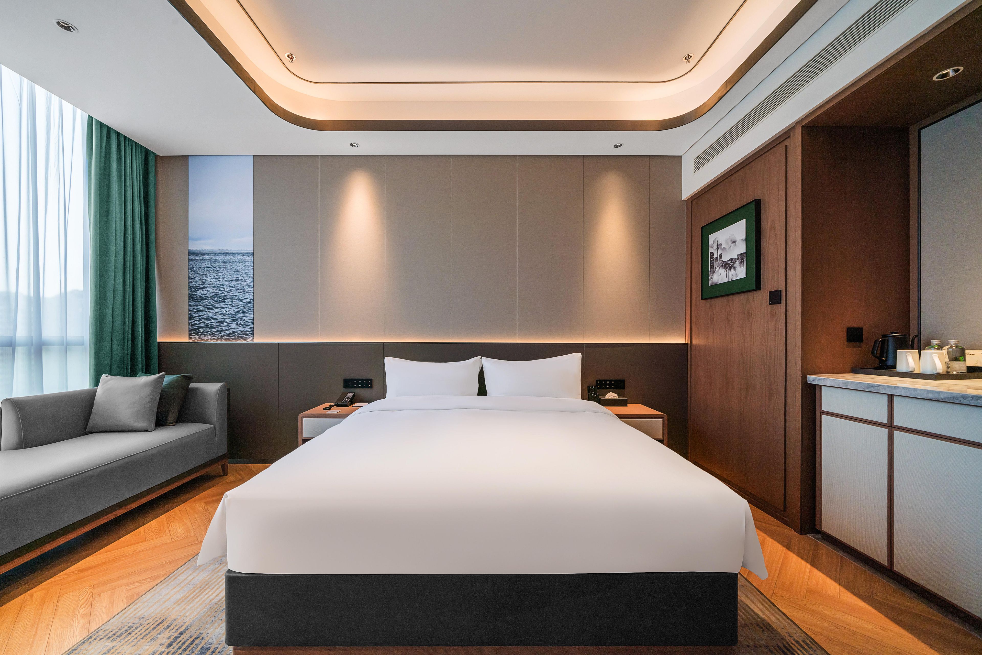 Habitación de hotel moderna con una cama grande, un sofá, un escritorio y vistas al mar.