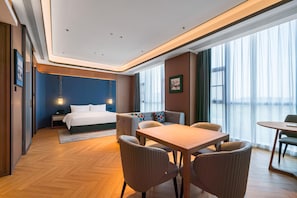A modern hotel room with a bed, a sofa, a dining table, and a view of the city. - Grand Madison Hotel Nantong Tongzhou High-tech (Nantong)