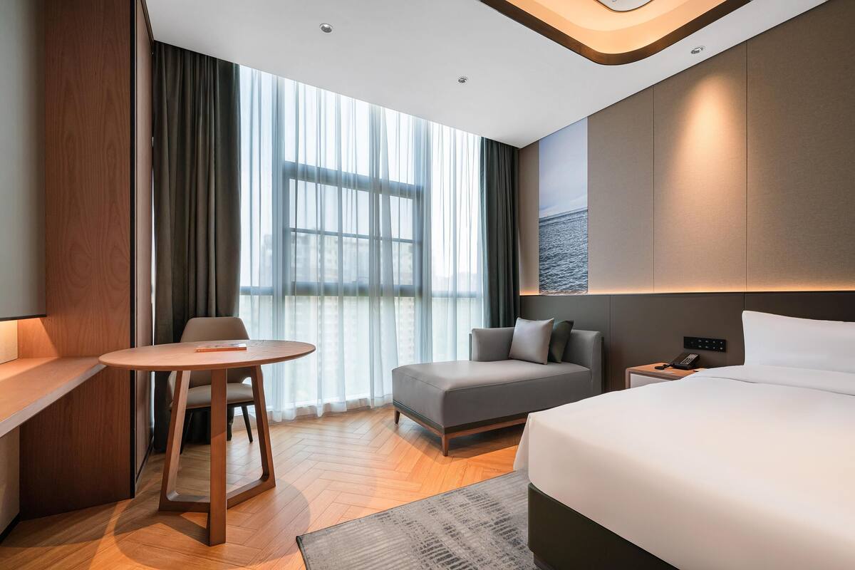 A modern hotel room with a large bed, a sofa, a small table, and a desk.