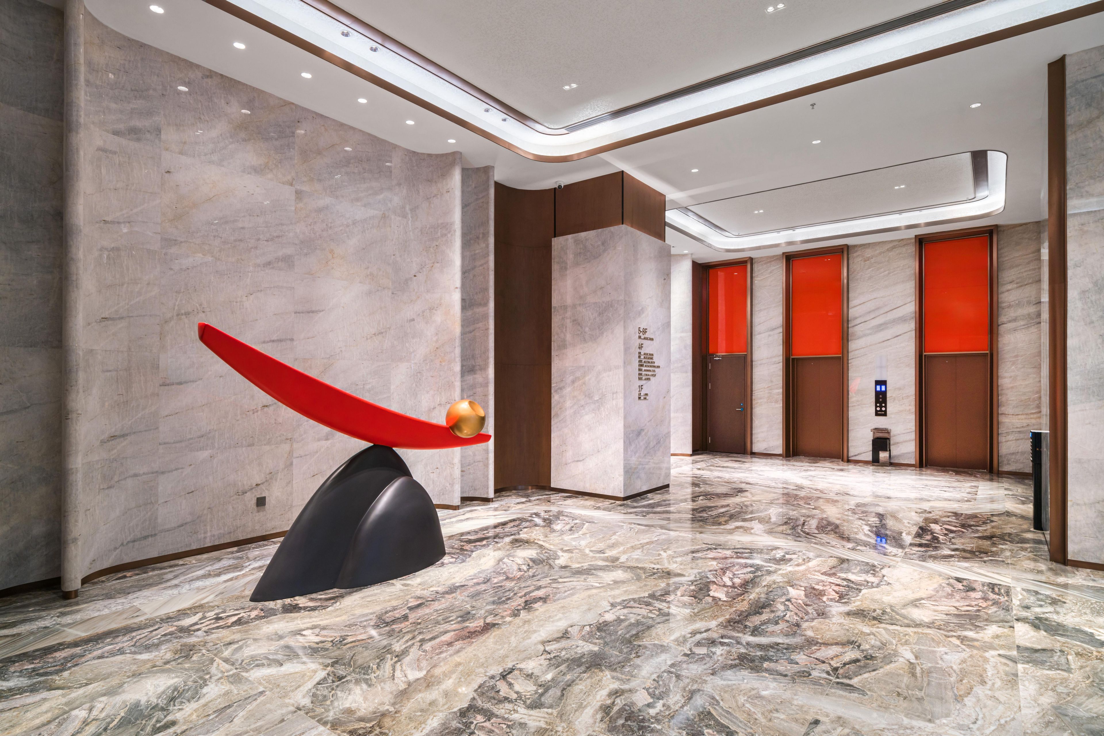 A modern lobby with marble flooring, a unique red sculpture, and a reception area with a digital display.
