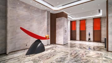 A modern lobby with marble flooring, a unique red sculpture, and a reception area with a digital display.
