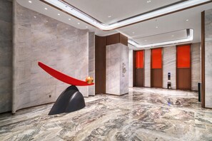 A modern lobby with marble flooring, a unique red sculpture, and a reception area with a digital display. - Grand Madison Hotel Nantong Tongzhou High-tech (Nantong)