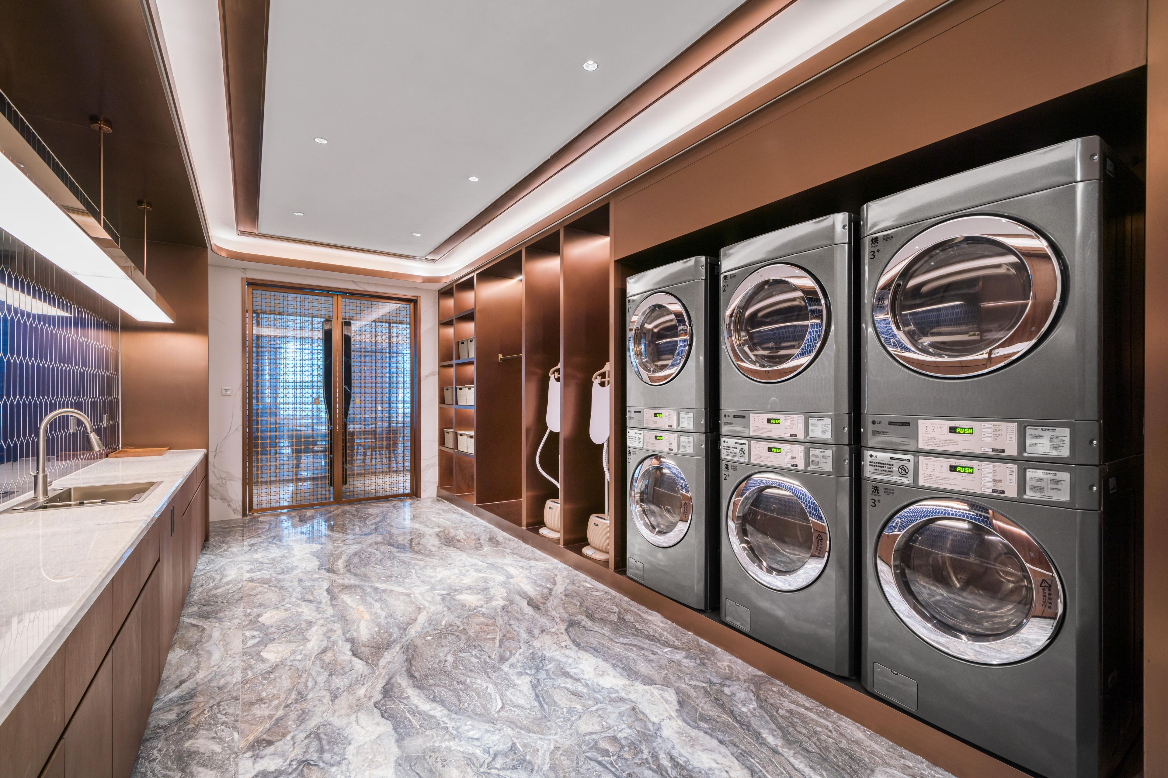 A modern laundry facility with four stacked washing machines, a marble-tiled floor, and a glass door leading to an outdoor area.