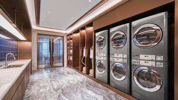 A modern laundry facility with four stacked washing machines, a marble-tiled floor, and a glass door leading to an outdoor area.