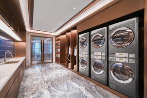 Un moderno cuarto de lavandería con cuatro lavadoras apiladas, piso de baldosas de mármol y una puerta de cristal que da a un área exterior.