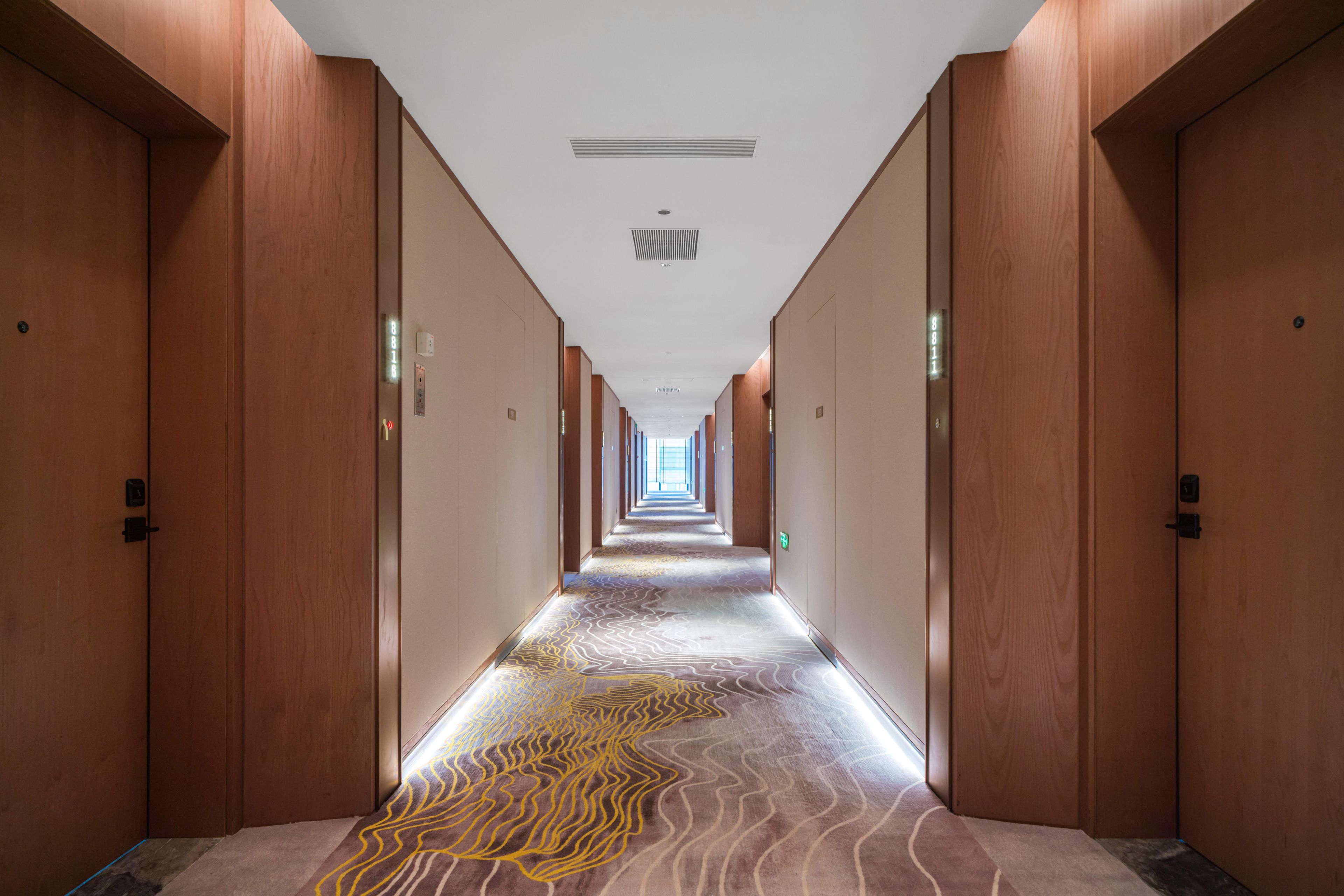 Un pasillo largo y estrecho con puertas de madera a ambos lados, que conduce a un extremo luminoso.