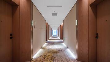 Un pasillo largo y estrecho con puertas de madera a ambos lados, que conduce a un extremo luminoso.