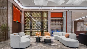 A modern lobby with a curved sofa, two round tables, and a decorative wall with vertical elements. - Grand Madison Hotel Nantong Tongzhou High-tech (Nantong)