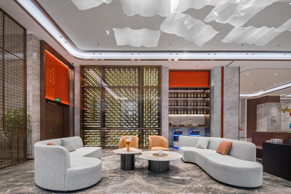 A modern lobby with a curved sofa, two round tables, and a decorative wall with vertical elements. - Grand Madison Hotel Nantong Tongzhou High-tech (Nantong)