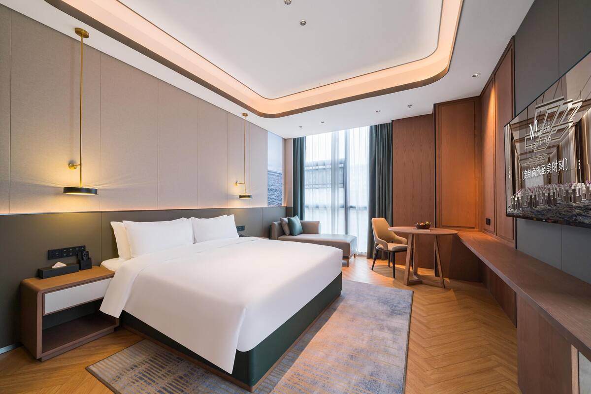 A modern hotel room with a large bed, bedside tables, a desk, and a seating area.
