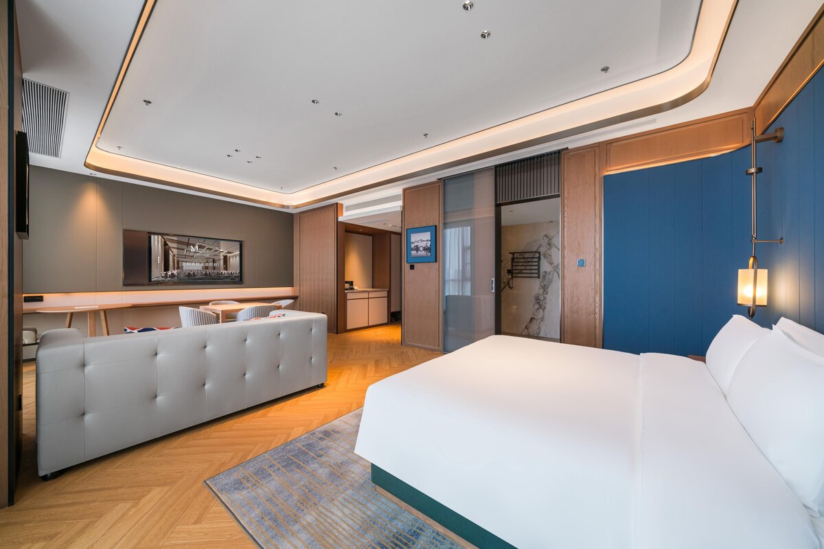 A modern hotel room with a large bed, a sofa, a desk, and a bathroom.