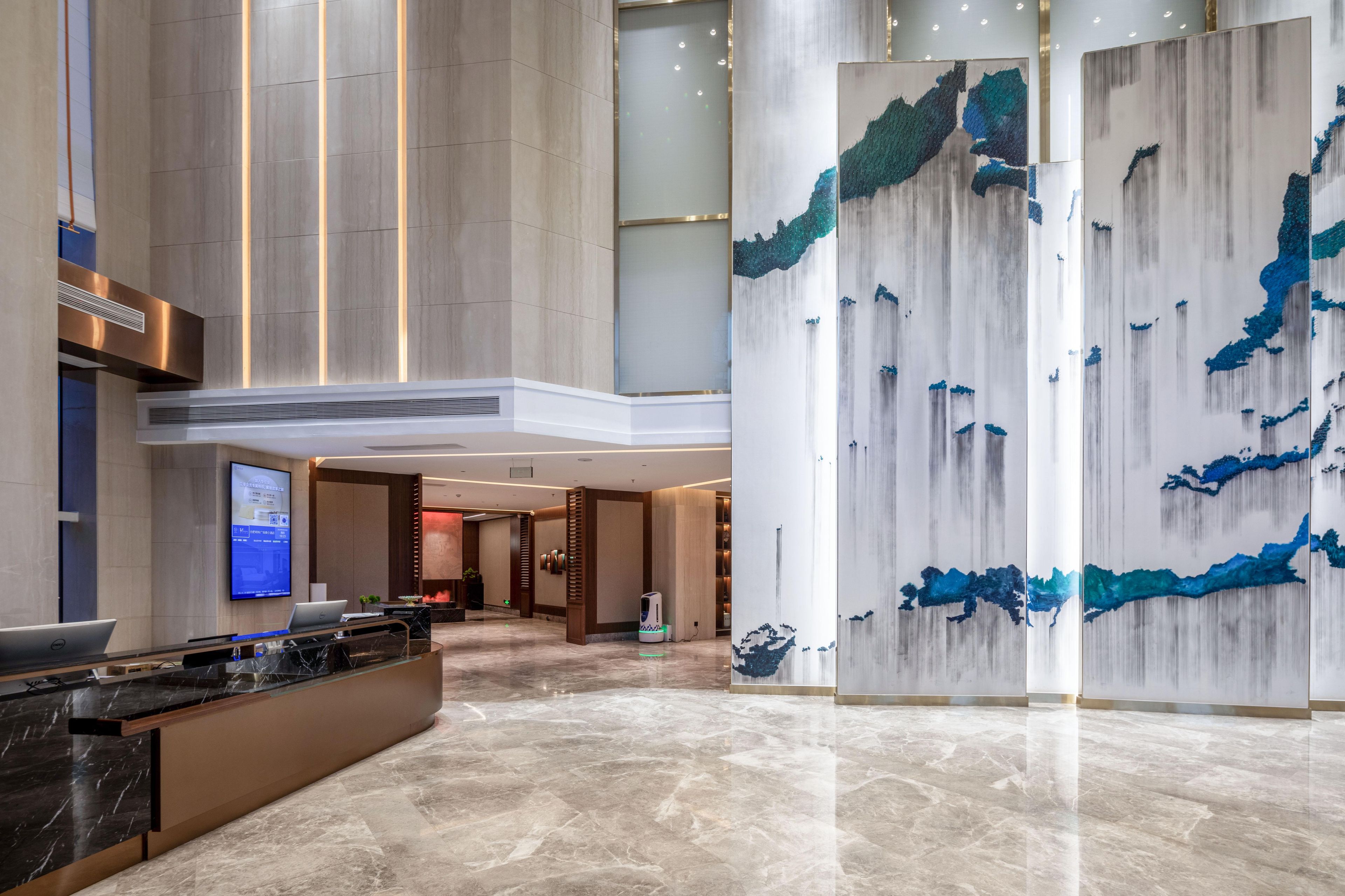 A spacious lobby with a reception desk, a large digital display, and a modern abstract wall art piece.