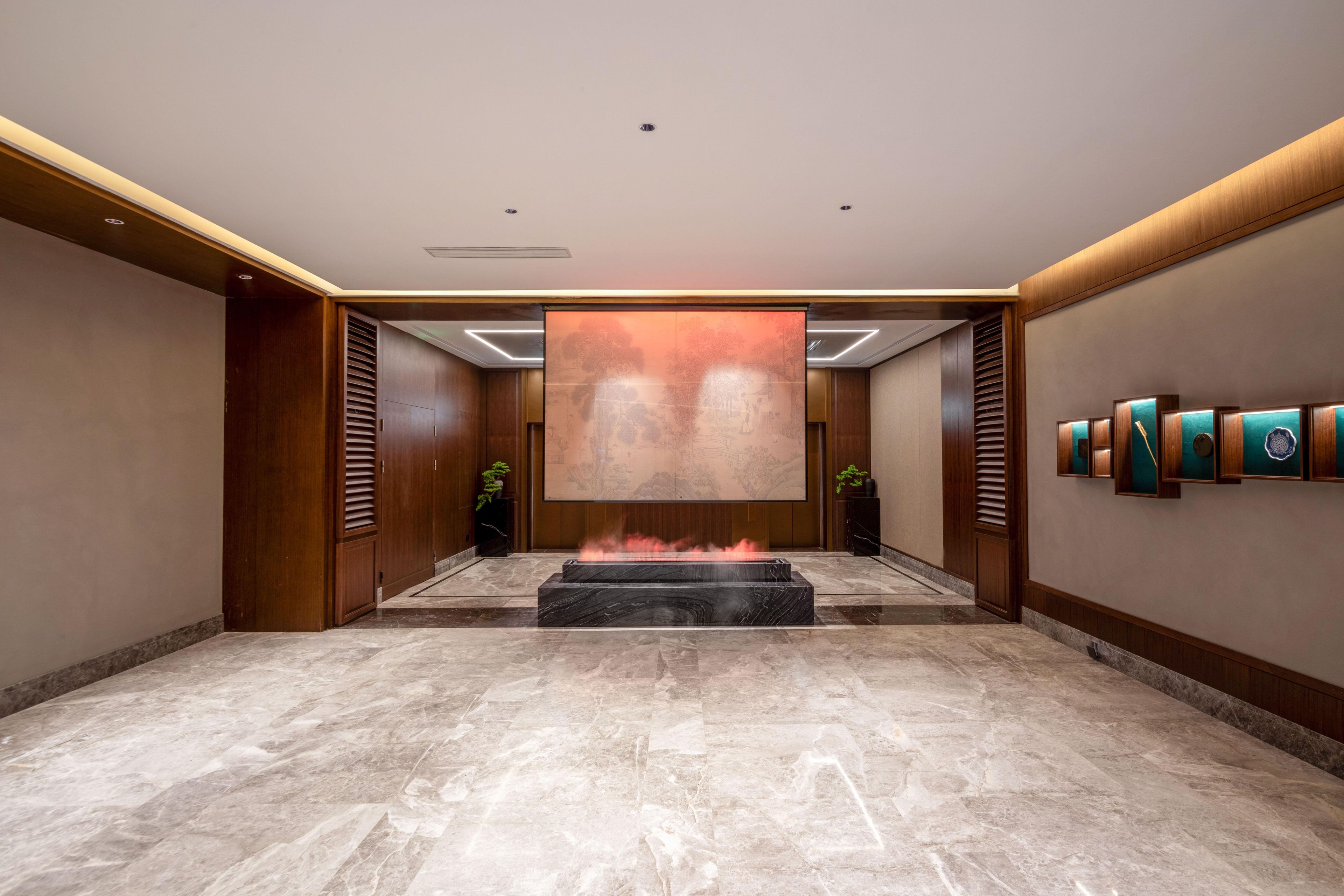 A spacious lobby with a marble floor, a large wall-mounted artwork, and a fire feature in the center.