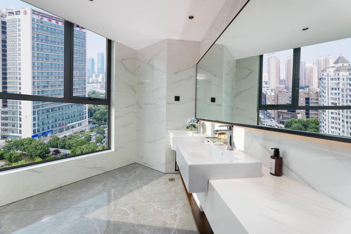 A modern bathroom with a large mirror, two sinks, and a view of a cityscape through large windows.