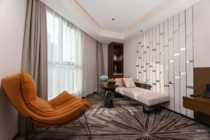 A hotel room with a sofa, a chair, a small table with flowers, a desk, and a decorative wall panel. - Madison Hotel Hefei 2nd Affiliated Hospital (Hefei)