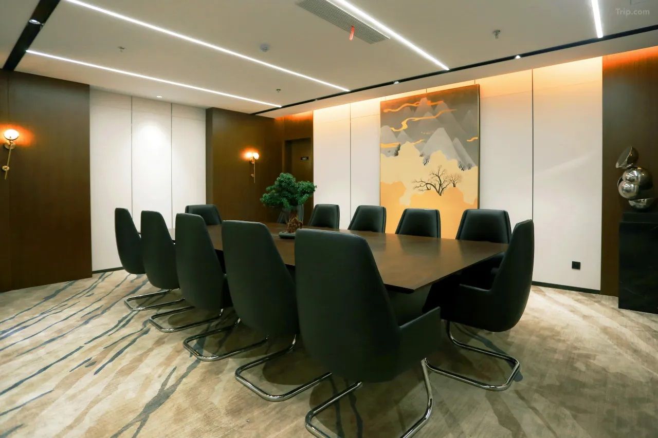 Uma sala de conferências com uma mesa comprida e oito cadeiras, uma parede decorativa com um mapa e duas luminárias fixadas na parede.