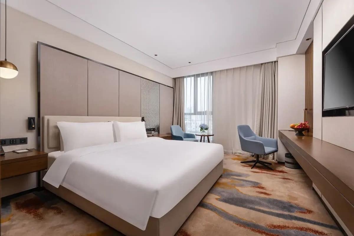 A modern hotel room with a large bed, a desk, a chair, and a TV.