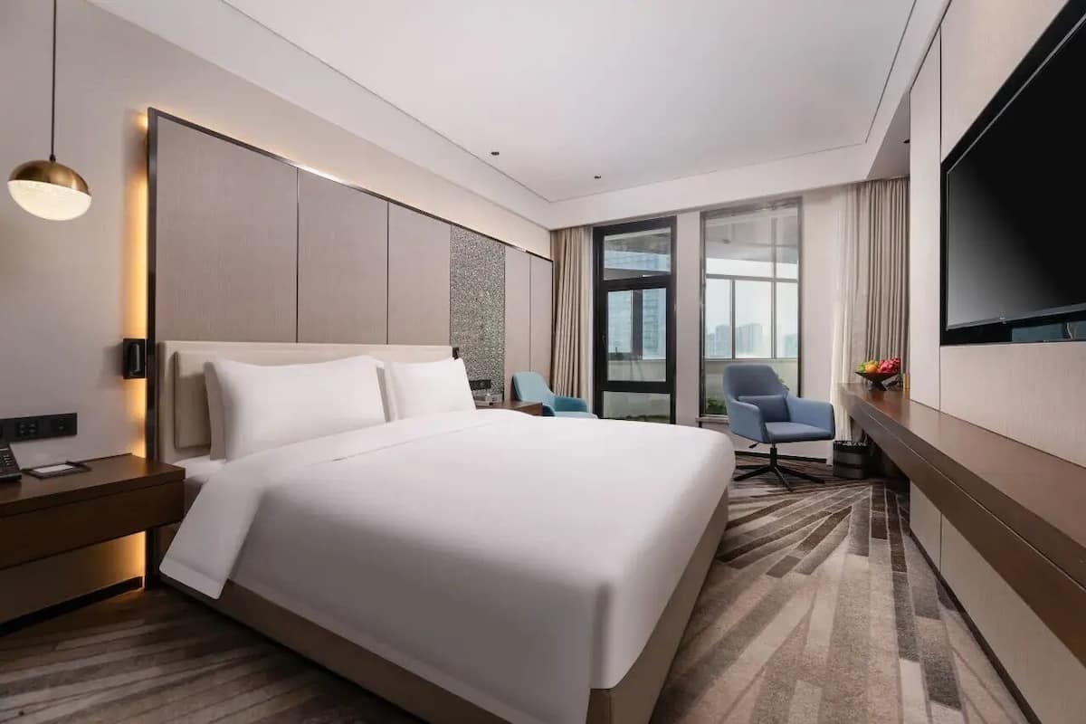 A modern hotel room with a large bed, a desk, a chair, and a TV.