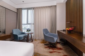 A hotel room with a bed, two armchairs, a small table with a vase, a fruit bowl, and a mirror on the wall. - Madison Hotel Hefei 2nd Affiliated Hospital (Hefei)
